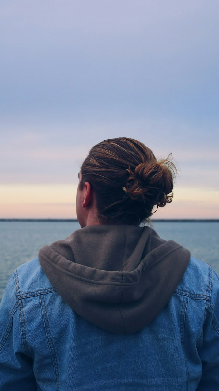 woman in blue denim jacket standing near body of water during daytime